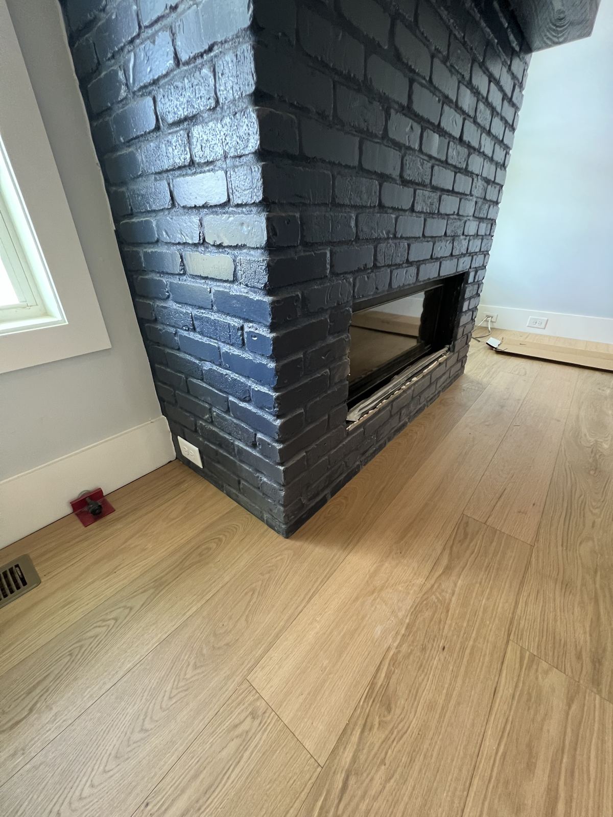 Light oak plank floor meeting a black painted brick fireplace