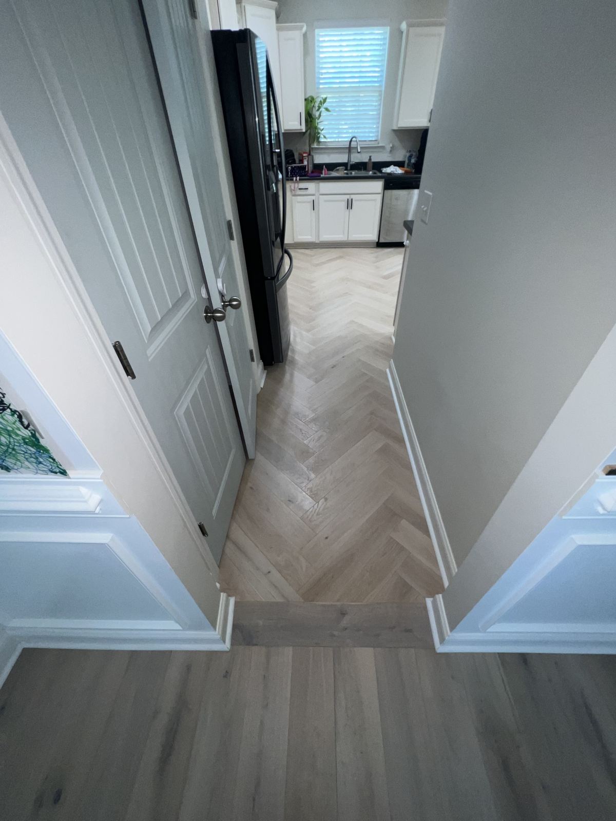 Light oak herringbone running from a hallway into a kitchen