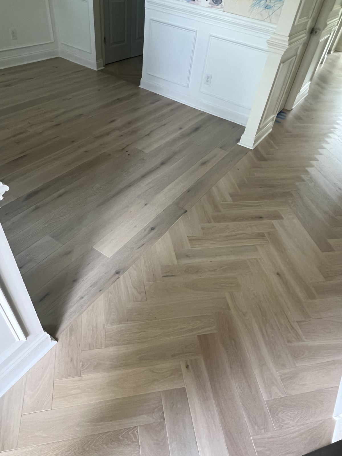 Light oak herringbone meeting a straight-plank floor at a doorway
