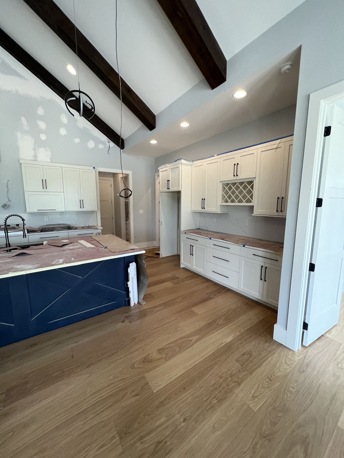 Wide-plank light oak floor in a new kitchen with white cabinets and a navy island