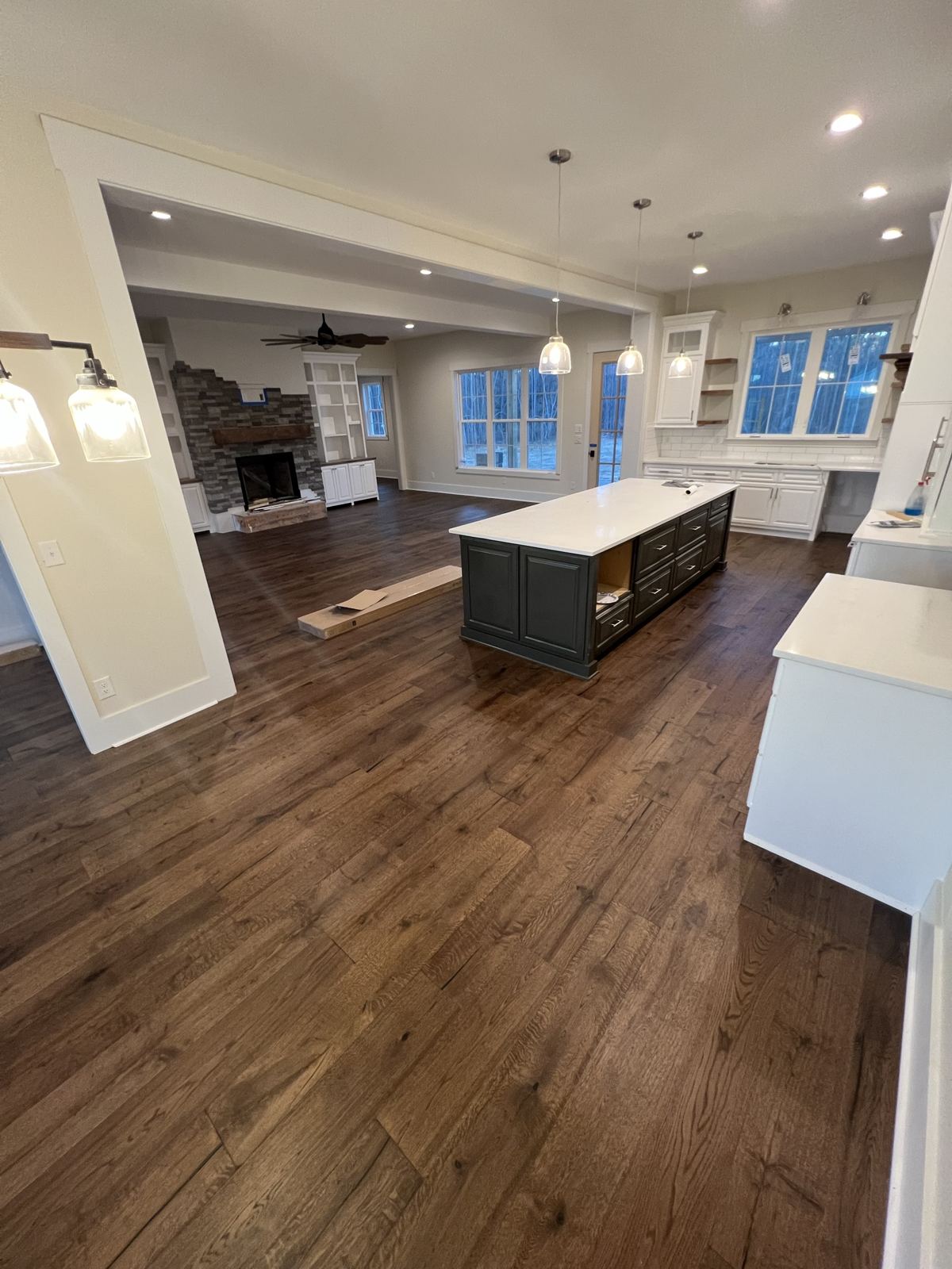 Dark wide-plank floor through an open kitchen and family room with a stone fireplace
